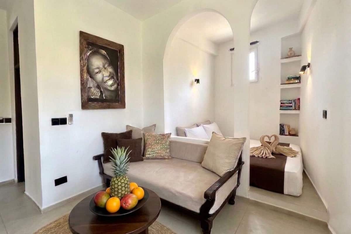 A living room with a sofa, a coffee table with fruit, a bookshelf, and a portrait on the wall.