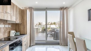 Eine moderne Küche mit Holzausstattung, einem Einbauofen und einer großen Schiebeglastür, die auf einen Balkon mit Sitzmöbeln führt.