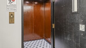 Interior de un ascensor con detalles de madera, un cartel de seguridad contra incendios y una placa metálica en la pared.