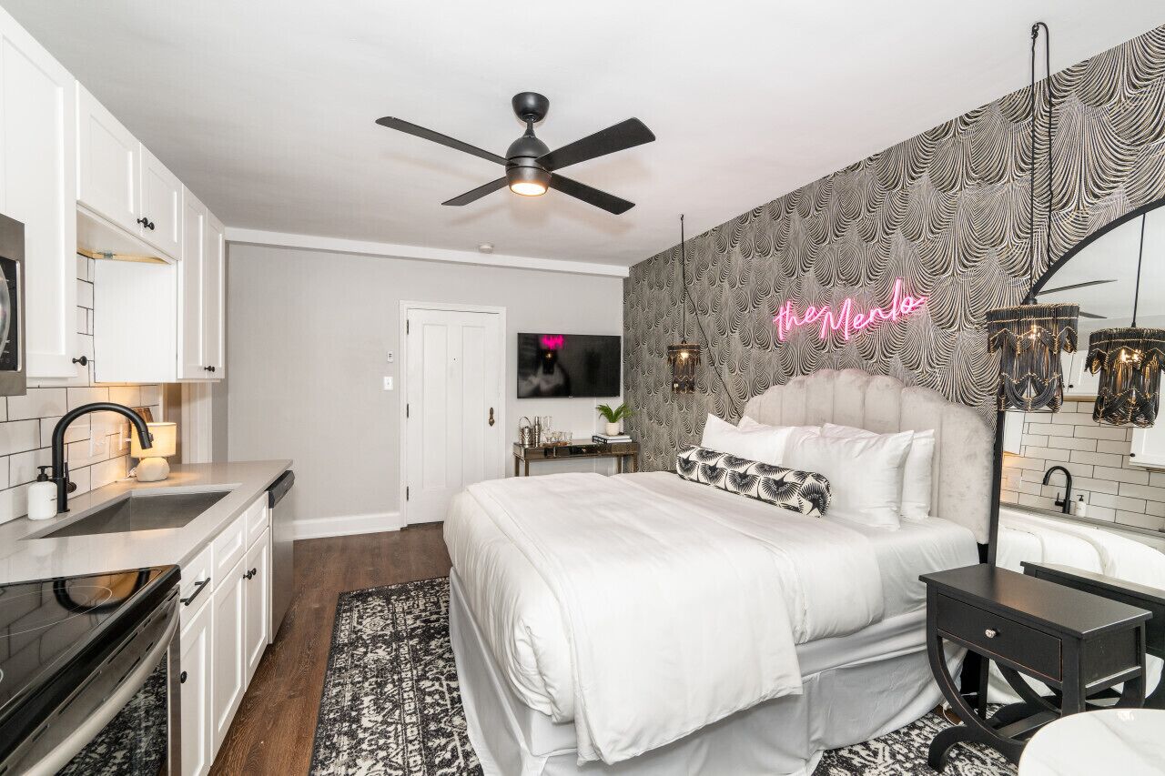 A modern bedroom with a large bed, a ceiling fan, a neon sign, and a patterned wall.