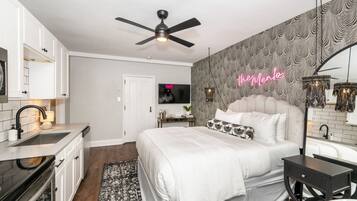 A modern bedroom with a large bed, a ceiling fan, a neon sign, and a patterned wall.