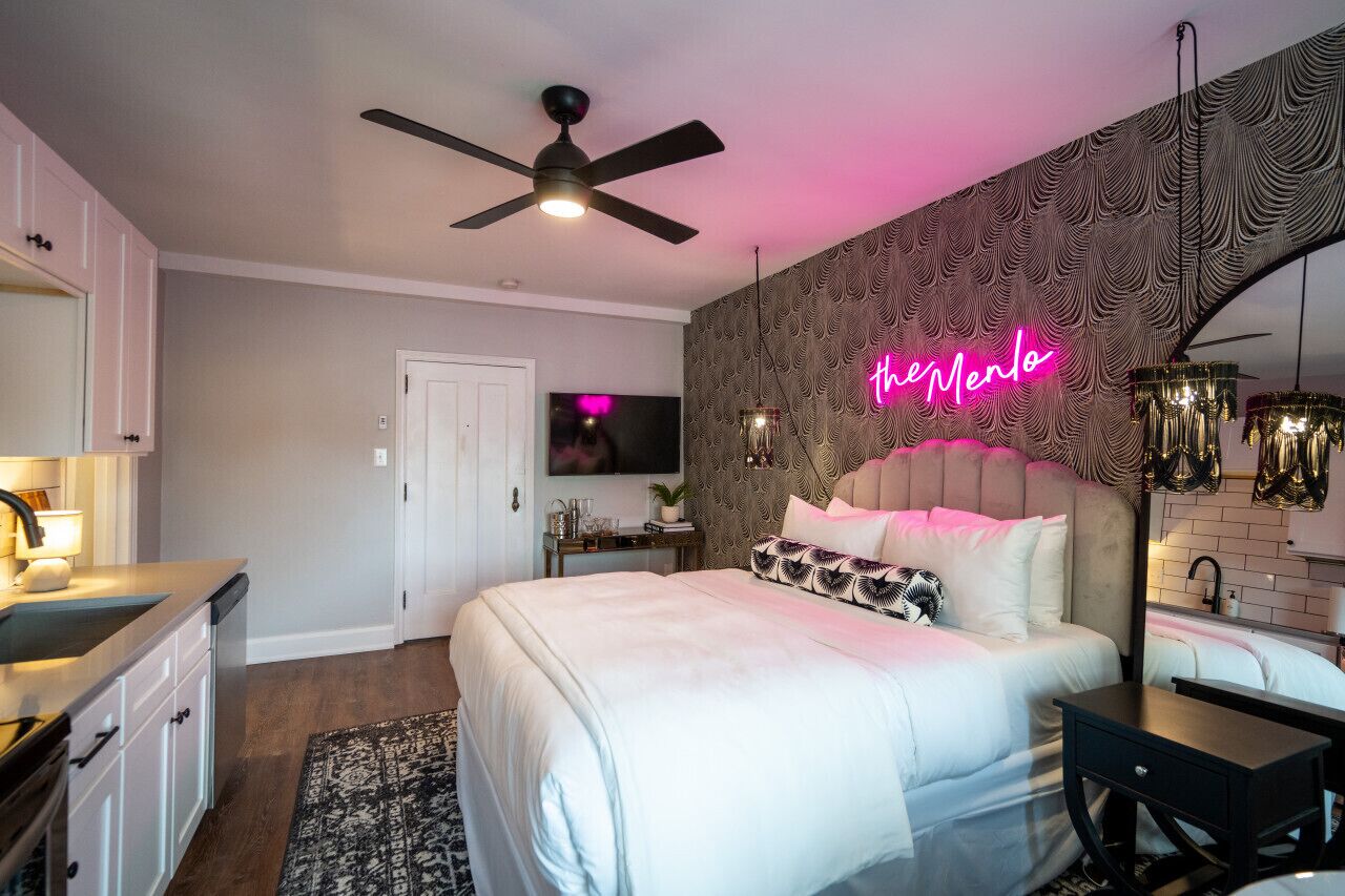 A modern bedroom with a bed, a ceiling fan, a neon sign, and a TV.