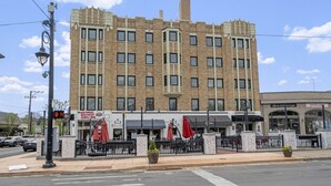 Un edificio de varios pisos con fachada de ladrillo, que cuenta con un restaurante en la planta baja con mesas al aire libre y un escaparate visible.