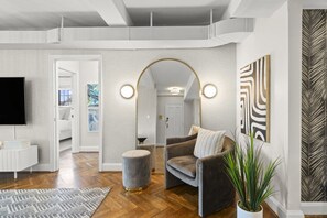 A modern living room with a grey sofa, a round mirror, and a flat-screen TV. - The Rookwood | Hyde Park (Cincinnati)