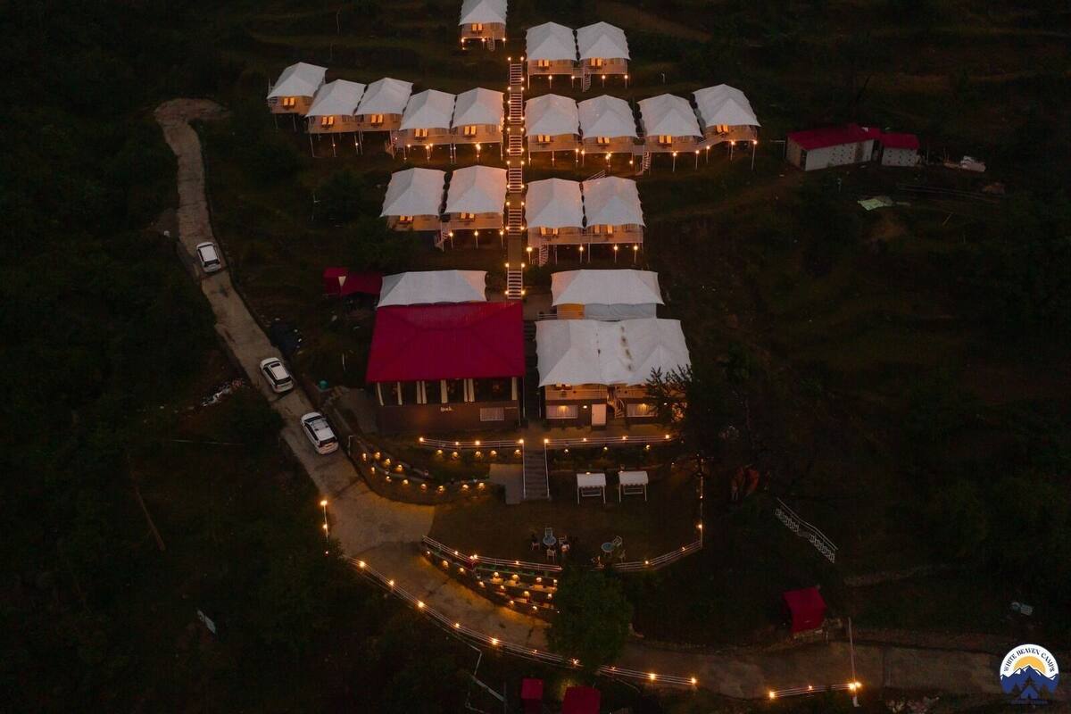 Vista aérea de un resort con varias construcciones en forma de cúpula, un edificio central con techo rojo y un sendero bien iluminado.