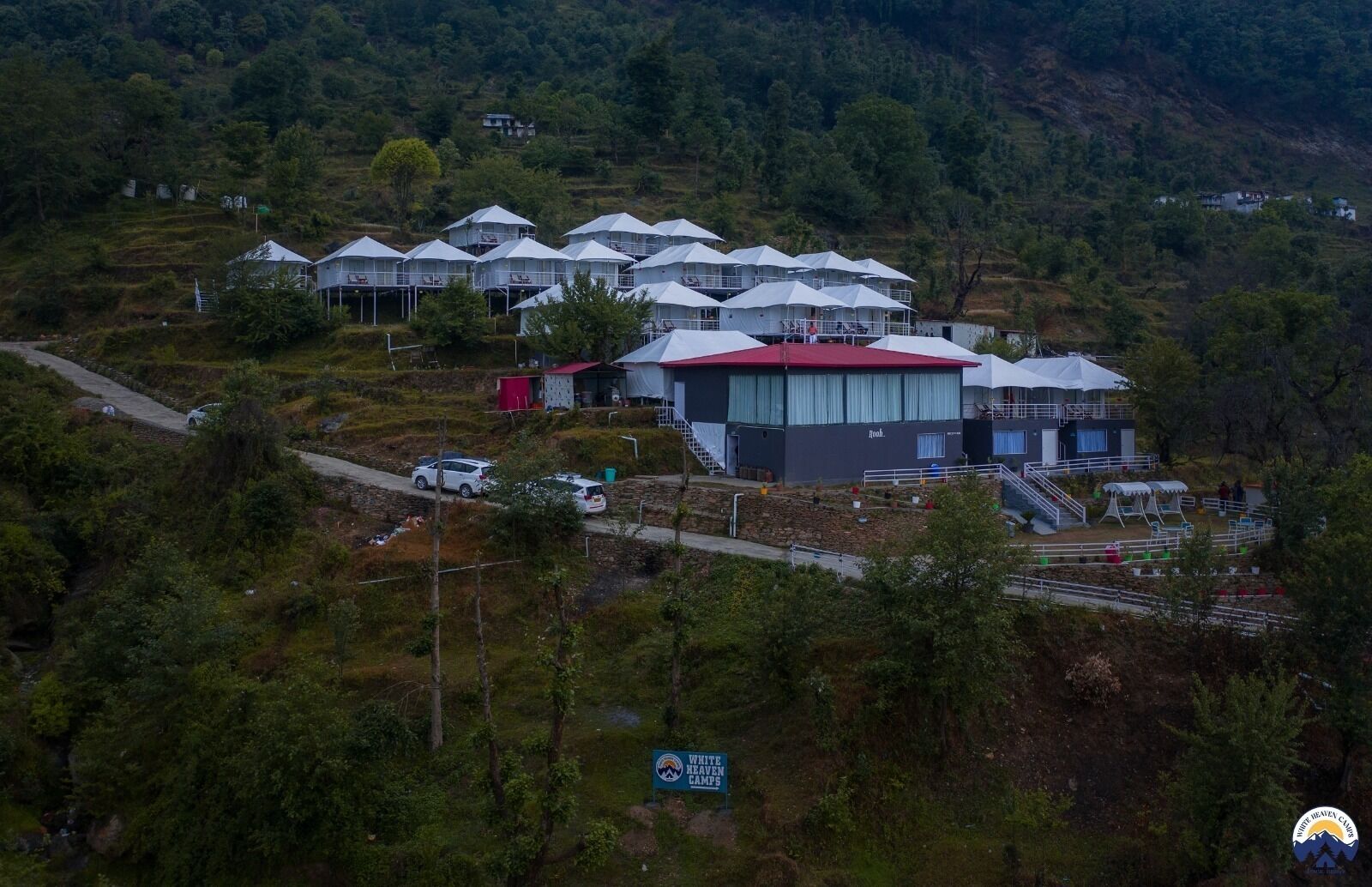 A series of white tents with red roofs, arranged in a cluster on a hillside.
