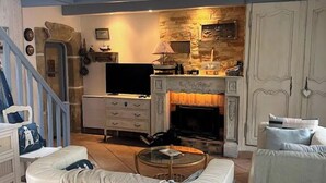 A living room with a curved white sofa, a coffee table, a fireplace, and a television. - Ty Zazou - Maison d'amis et de famille (Lanvéoc)