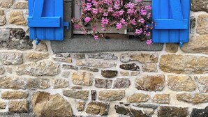 A stone building with a window featuring blue shutters and pink flowers. - Ty Zazou - Maison d'amis et de famille (Lanvéoc)