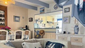 A cozy living room with a sofa, cushions, and a dining area with chairs and a table. - Ty Zazou - Maison d'amis et de famille (Lanvéoc)