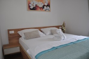 Un lit bien fait, avec du linge de lit blanc, un plaid bleu vif et une tête de lit en bois.
