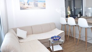 Una sala moderna con un sofá beige, una mesa de centro de cristal y sillas blancas.