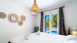 Habitación de hotel con cama, lámpara colgante, ventana con vista a una piscina y una silla junto a la ventana.