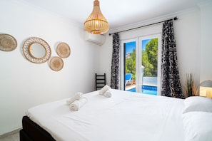 Une chambre d’hôtel avec un lit, un luminaire suspendu, une fenêtre donnant sur une piscine et une chaise près de la fenêtre.