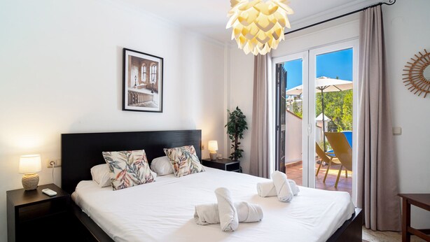 Habitación de hotel con cama, mesita de noche, cuadro en la pared, lámpara de techo y vistas al exterior.