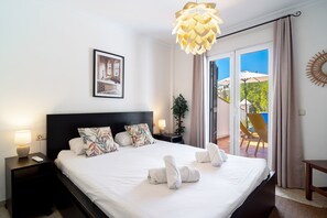 Ein Hotelzimmer mit Bett, Nachttisch, Wandbild und Deckenleuchte, mit Blick ins Freie.