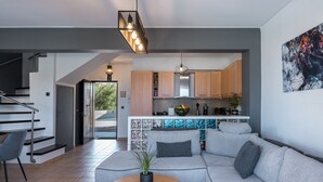 A modern living room with a grey sofa, a wooden coffee table, and a staircase leading to an upper floor. - Steps from Maleme beach, walking distance to shops, private pool! (Chania)