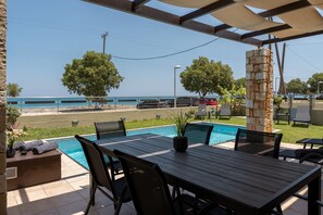 Ein Poolbereich mit Holztisch und Stühlen, einer Steinsäule und Blick auf das Meer.