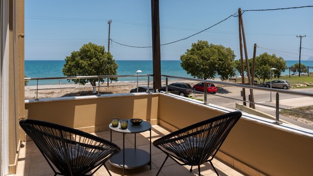 A balcony with two chairs and a small table, overlooking a beach and the sea. - Steps from Maleme beach, walking distance to shops, private pool! (Chania)