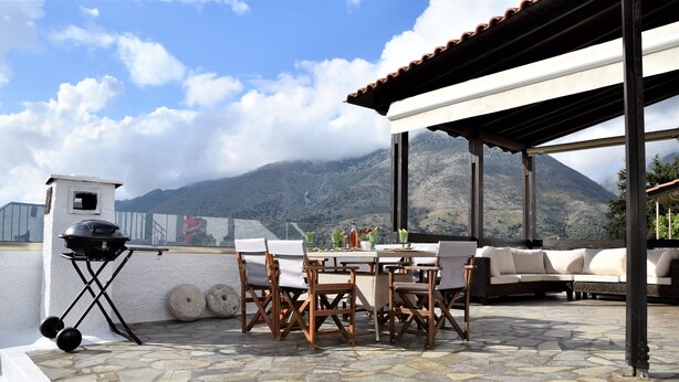 Une terrasse extérieure avec une table et des chaises, un barbecue et une vue sur une montagne.
