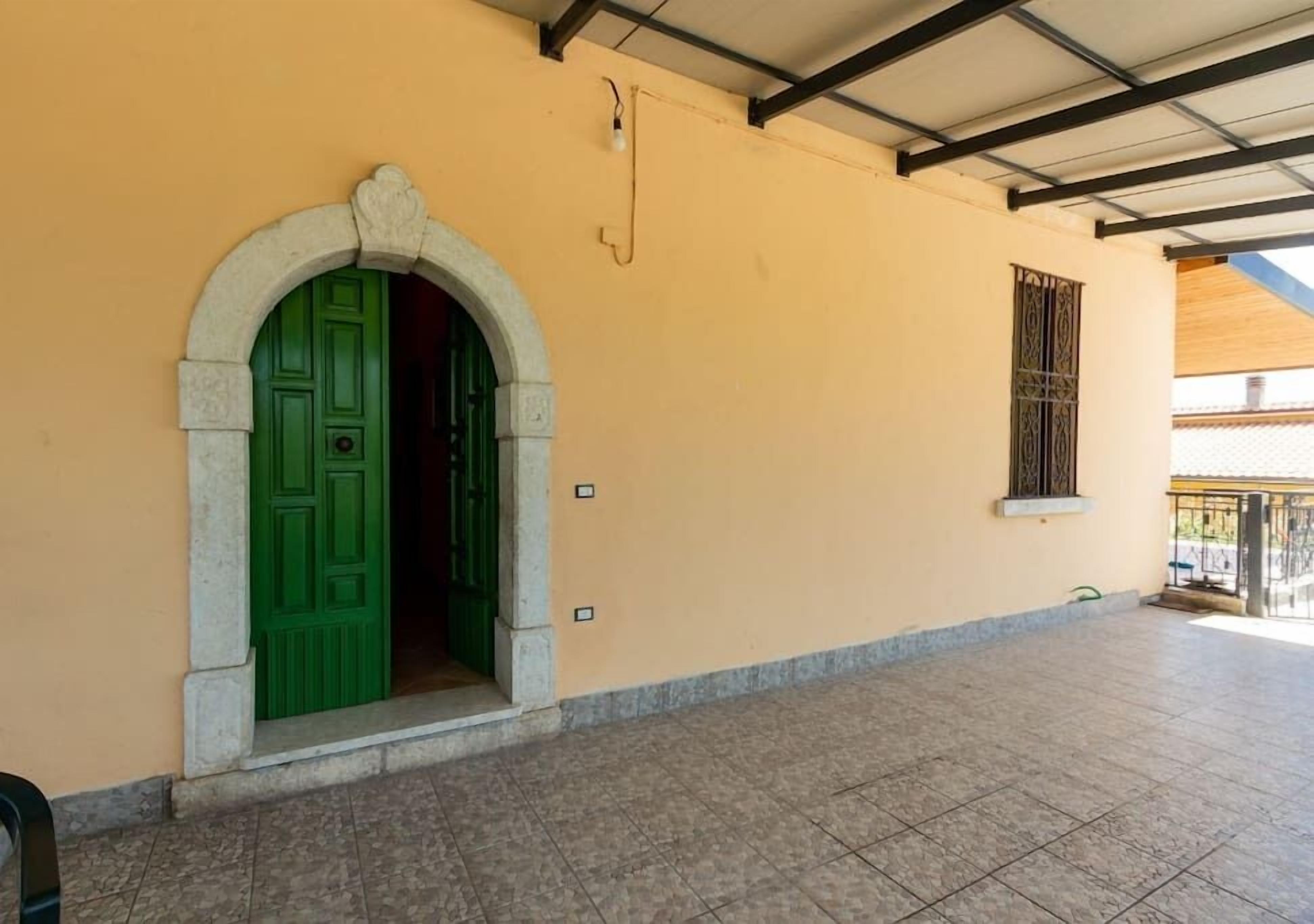 Edifici amb una porta verda, un paviment de rajoles i una barana metàl·lica.