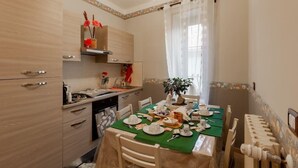 A dining area with a table set for a meal, a kitchen area with cabinets and a countertop, and a window with curtains.
