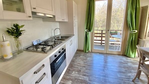 A kitchen with white cabinets, a gas stove, an oven, and a window with green curtains. - Cozy farmhouse in the mountains. Animals are welcome (Toscolano Maderno)