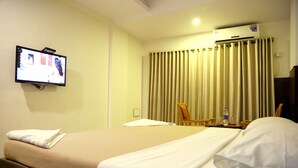 Una habitación de hotel con cama, televisión instalada en la pared, aire acondicionado y una ventana con cortinas.