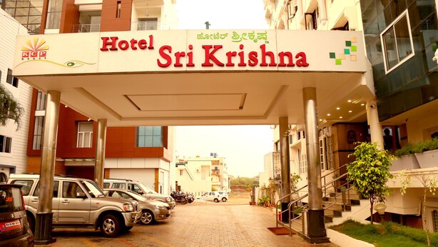 Hotel Sri Krishna con letrero, coches aparcados y una escalera que lleva a la entrada.