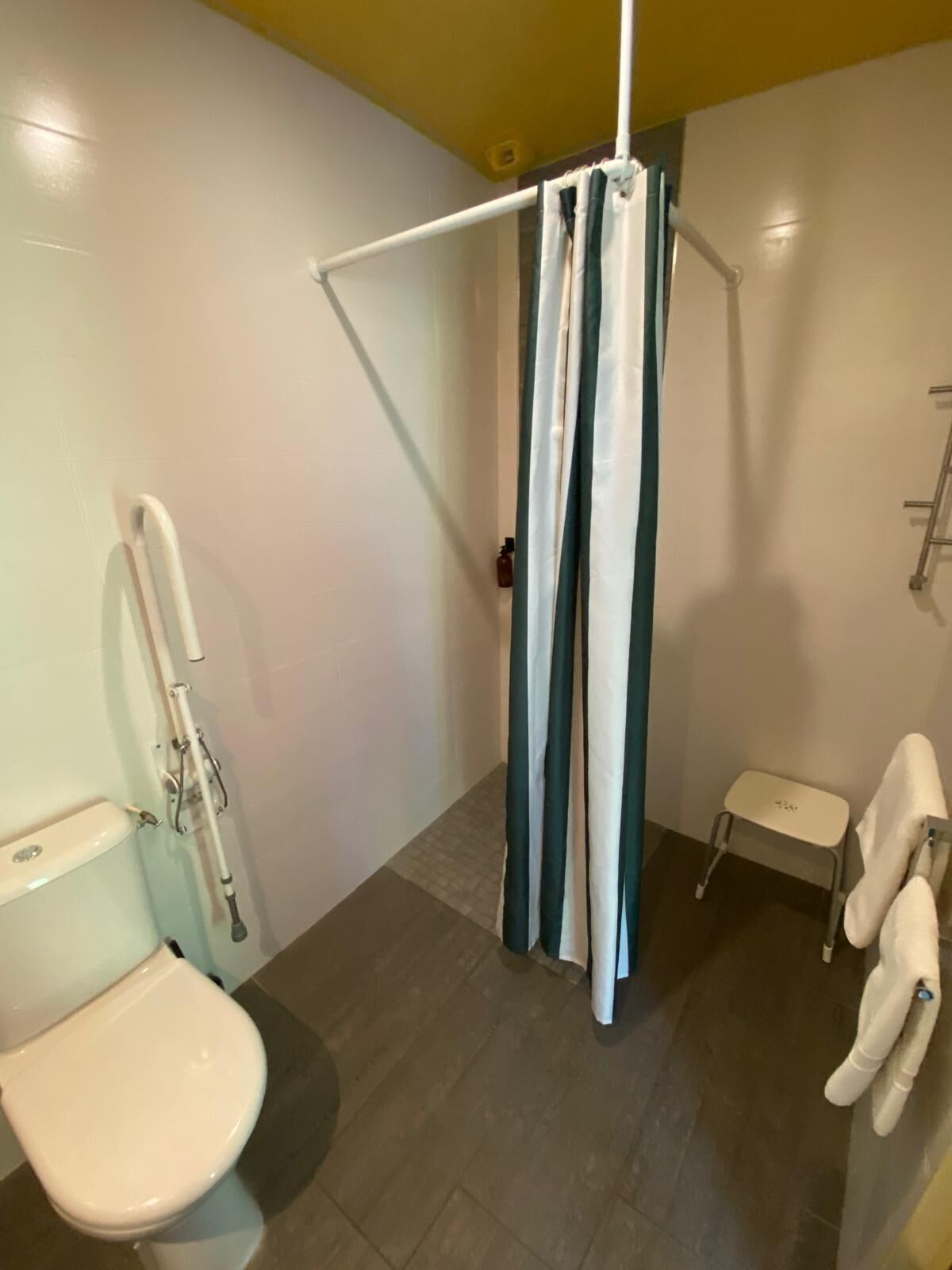 A bathroom with a white toilet, a shower curtain, a small white stool, and a towel rack.