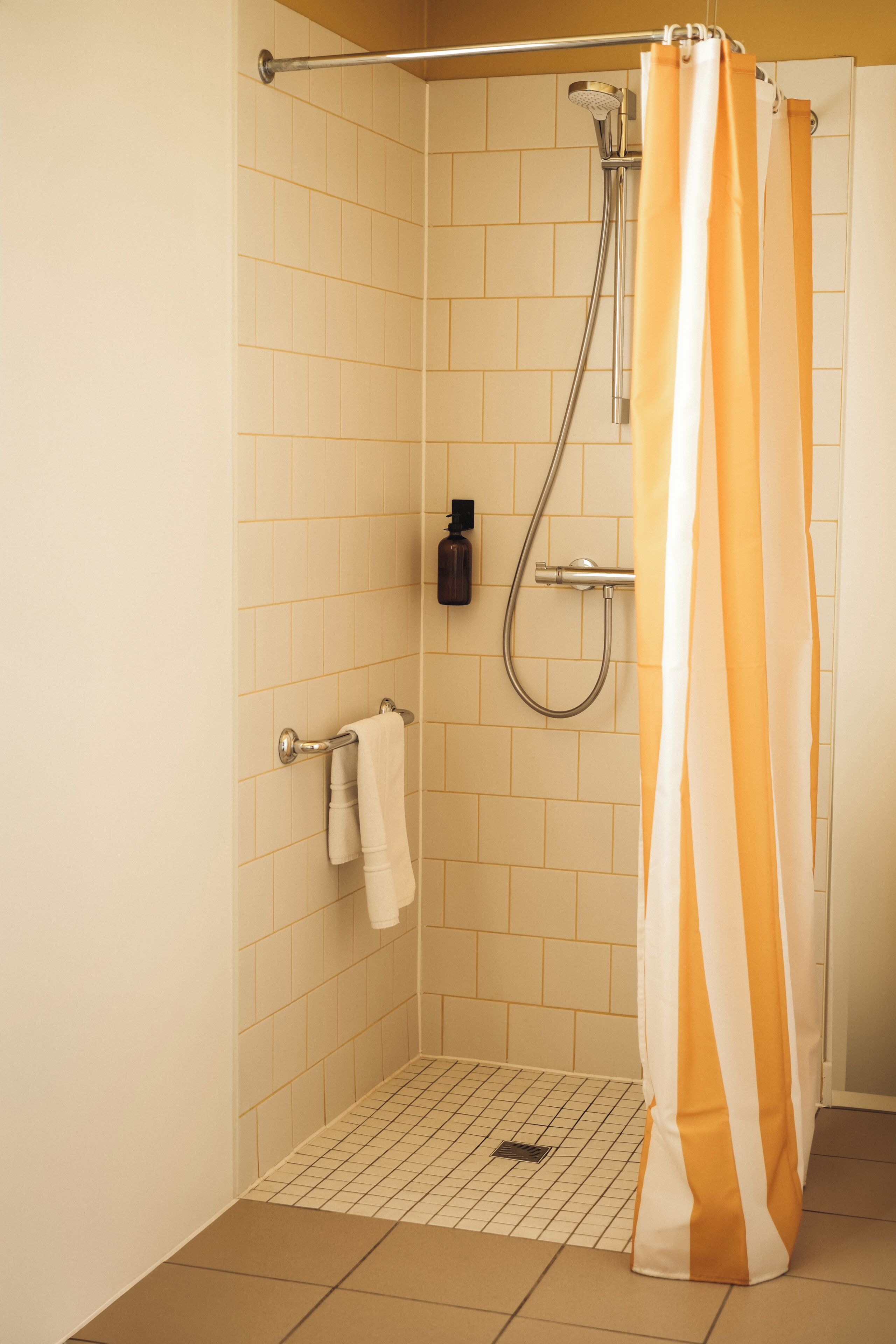 A shower with a striped curtain, a towel rack, and a handheld showerhead.