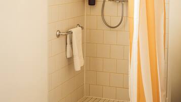 A shower with a striped curtain, a towel rack, and a handheld showerhead.