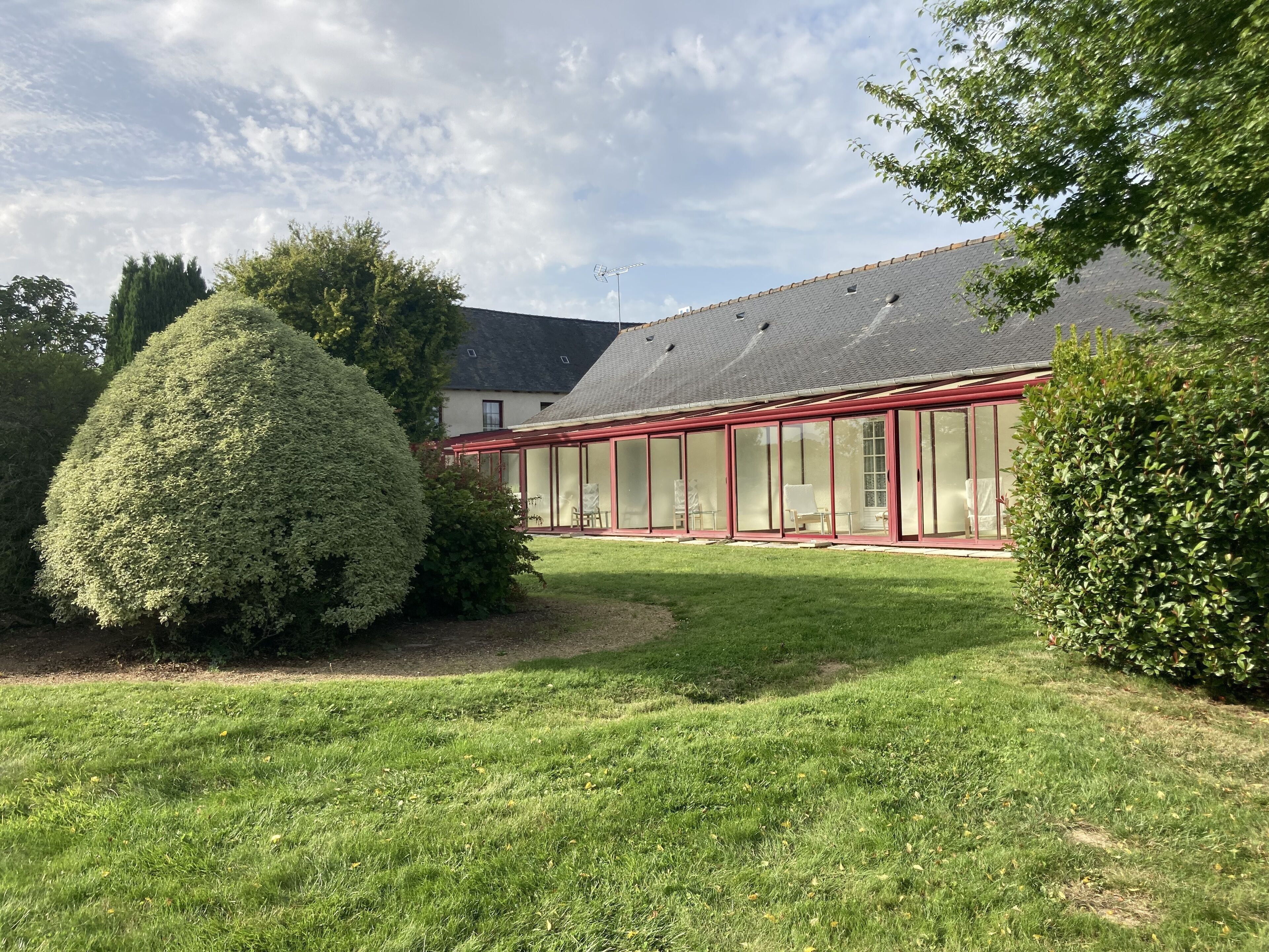 Een gebouw met een glazen conservatorium, een verzorgd gazon en een grote, netjes bijgesnoeide struik.