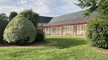 Een gebouw met een glazen conservatorium, een verzorgd gazon en een grote, netjes bijgesnoeide struik.