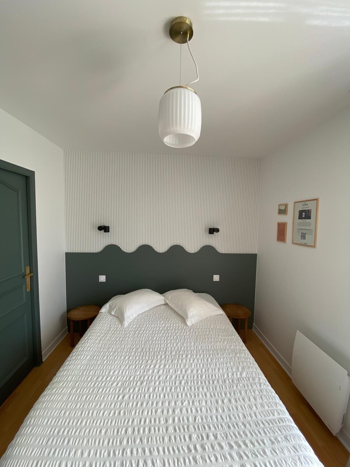 A bedroom with a bed, two bedside tables, a headboard, a wall-mounted light fixture, and a door.
