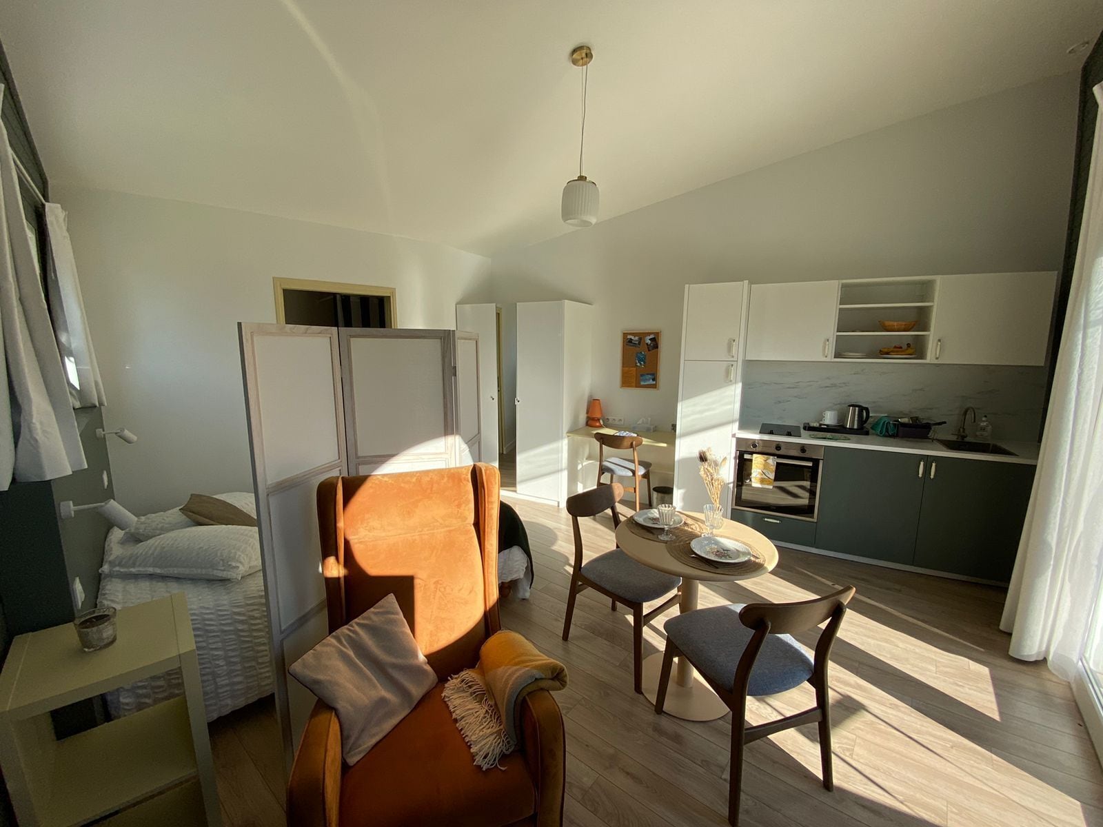 Um espaço de estar compacto com cama, sofá, mesa de jantar com cadeiras, cozinha e uma pequena janela.