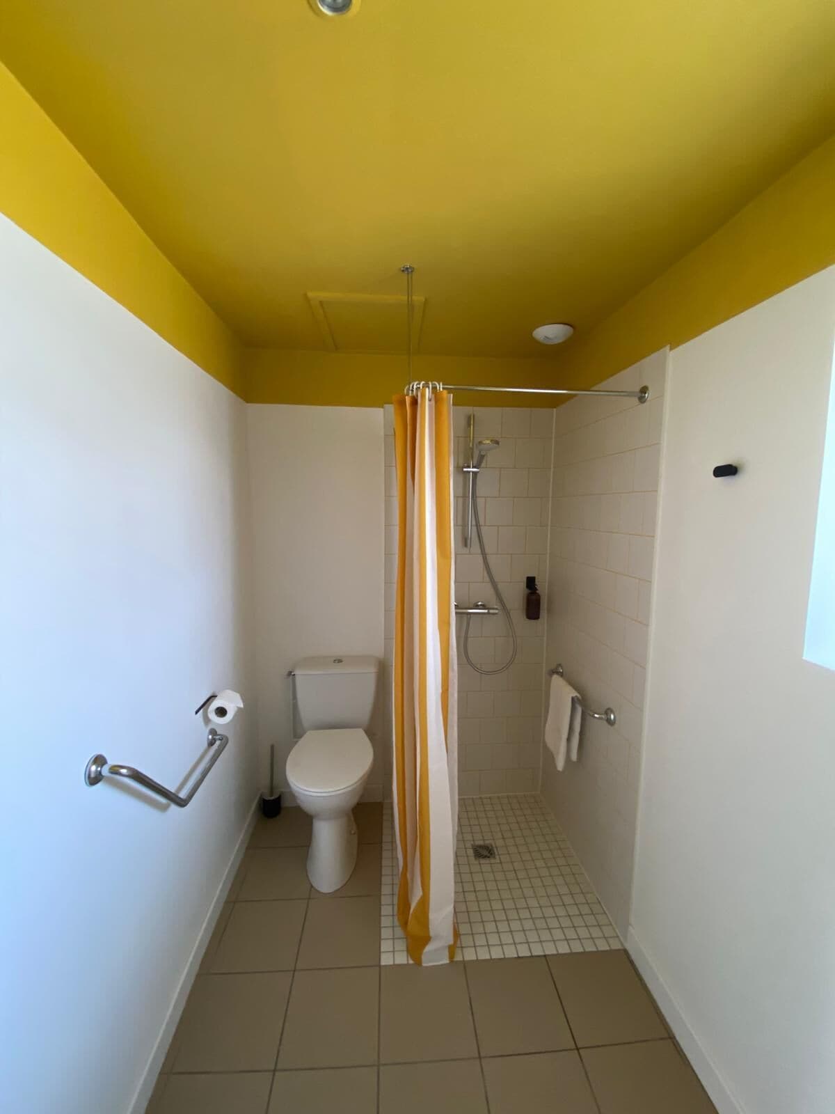 Baño pequeño con inodoro, ducha y techo amarillo.