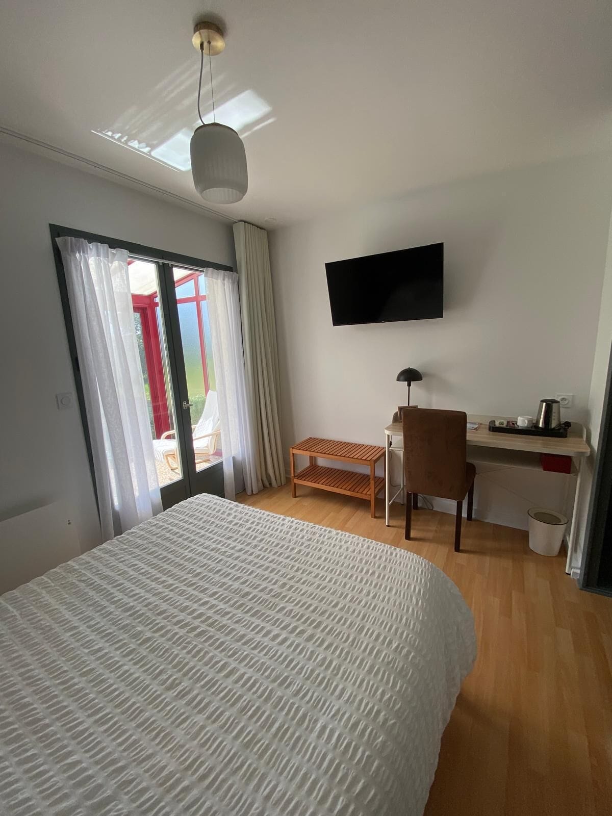 Habitación de hotel con una cama grande, un escritorio con una silla, un televisor montado en la pared y una ventana con cortinas.