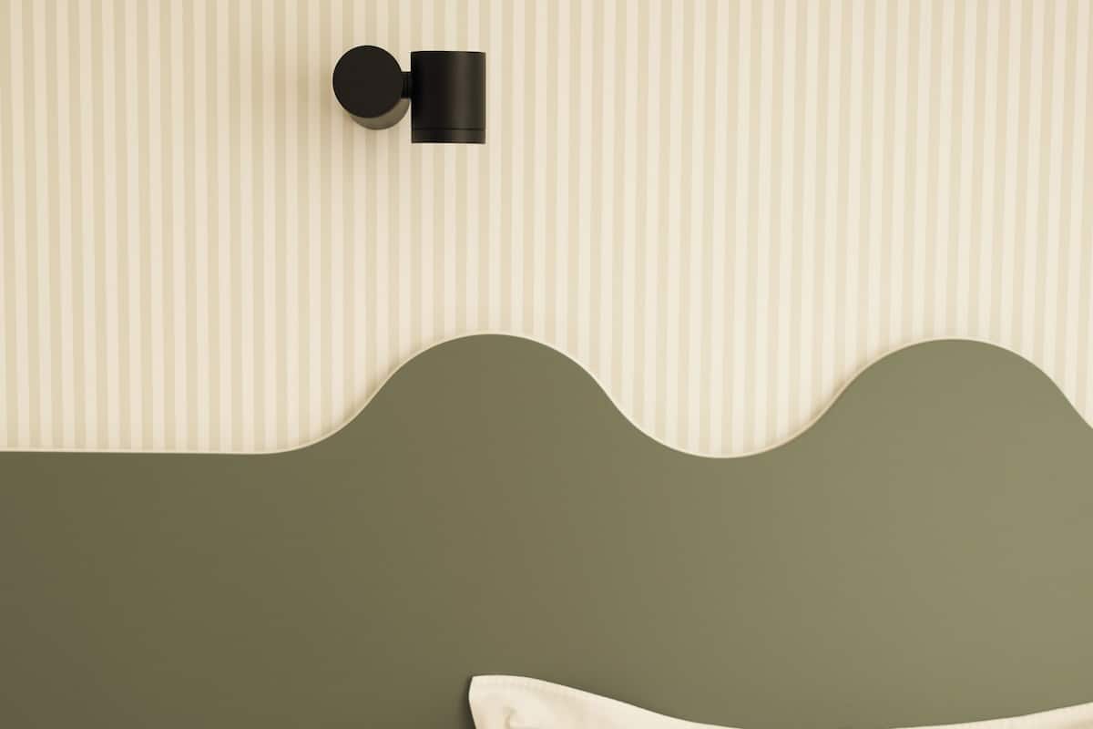 A bed with a green headboard, a round wooden stool, and a wall-mounted light fixture.