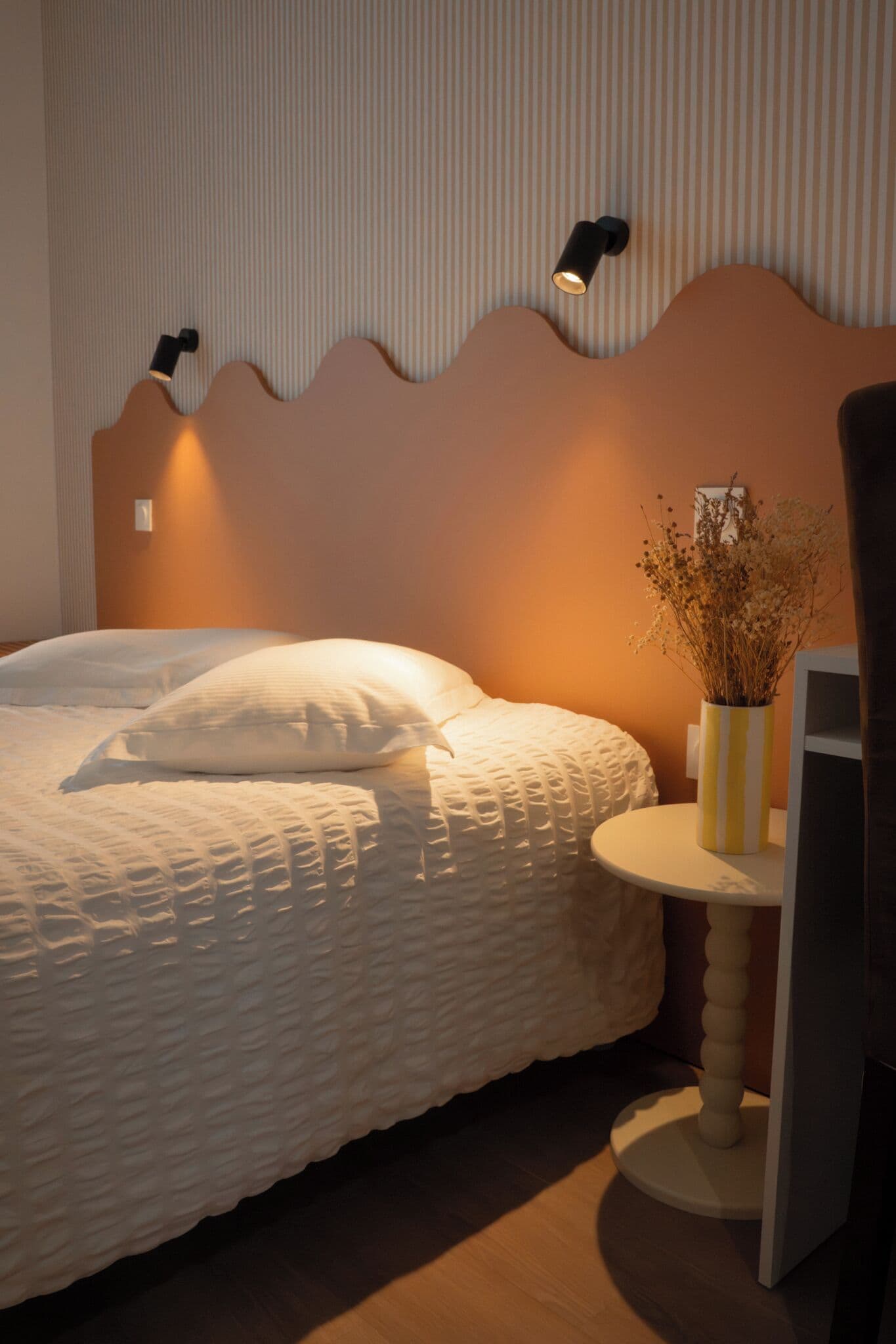 A bedroom with a bed, a bedside table with a lamp, and a wall-mounted light fixture.