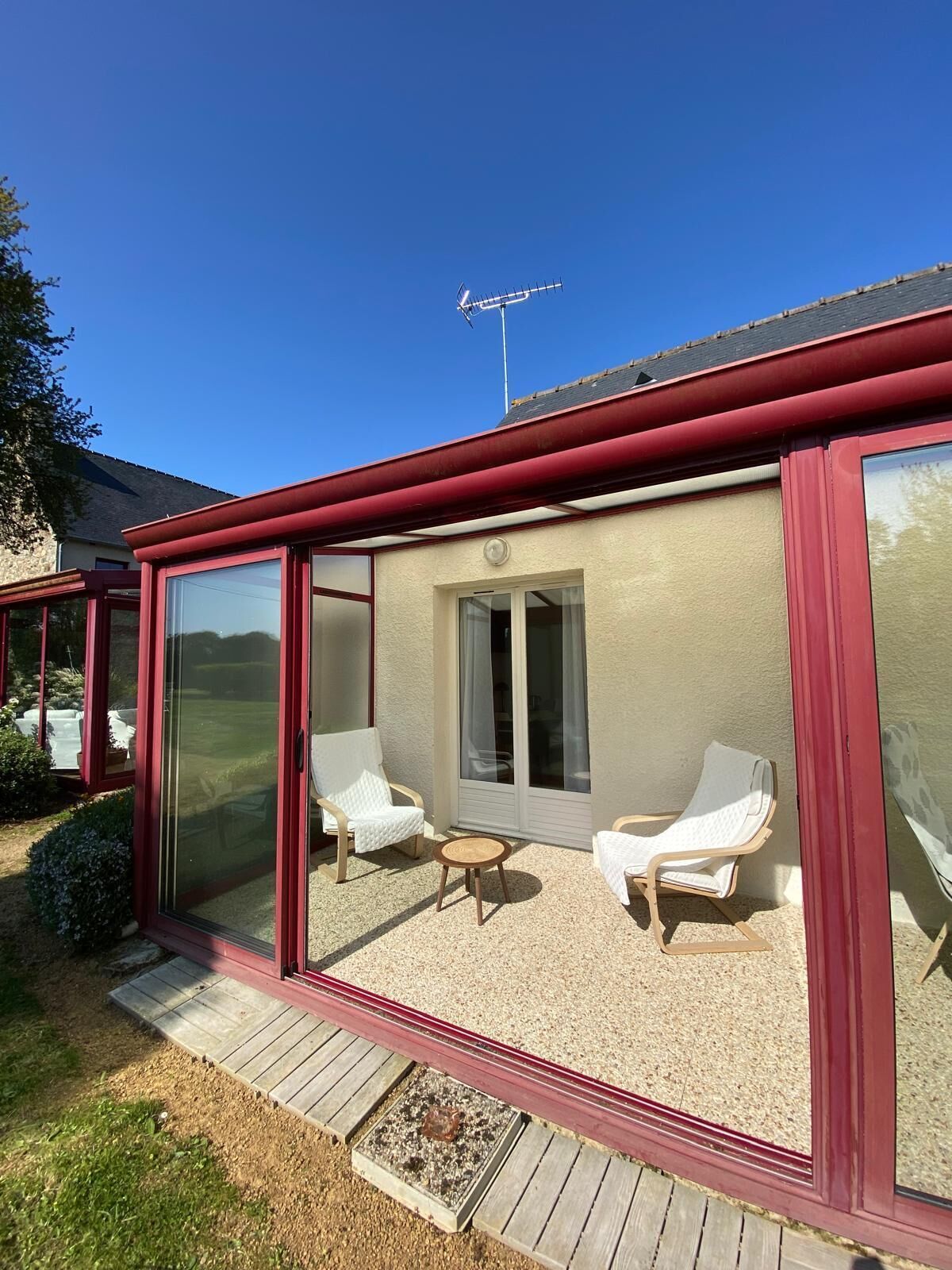 A covered patio area with two white lounge chairs, a small round table, and a sliding glass door leading to an outdoor space.