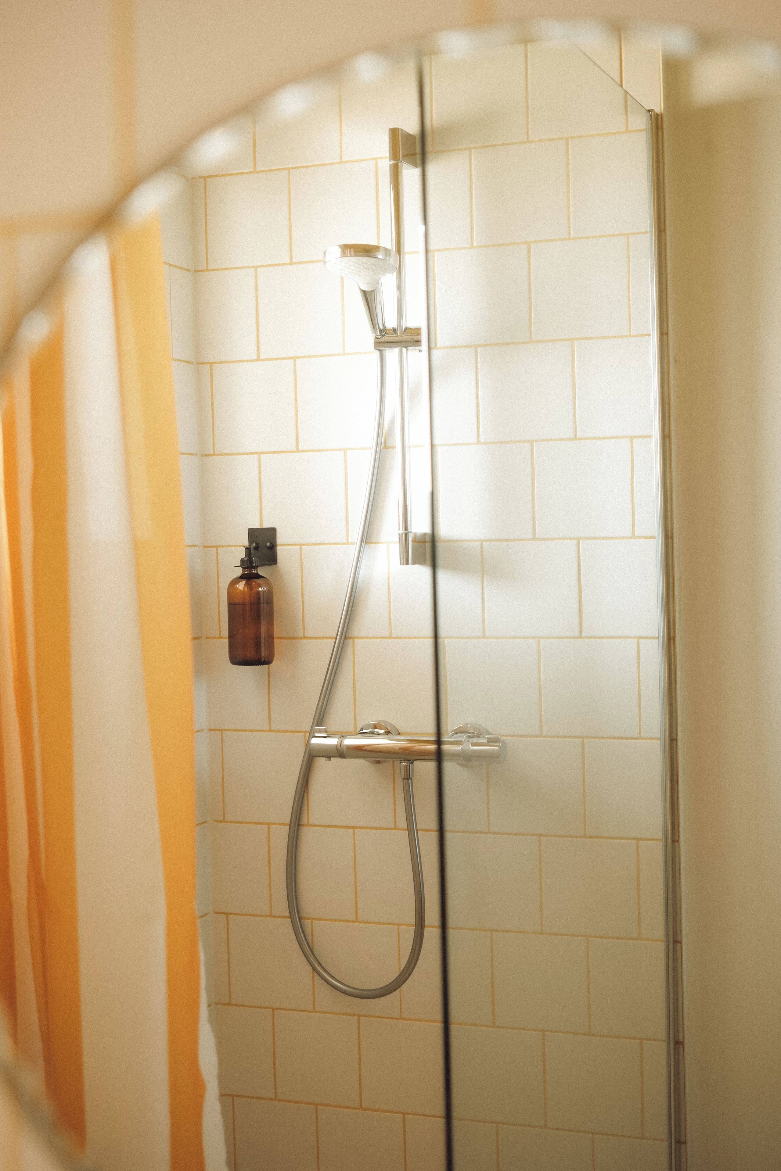 A shower with a glass door, a handheld showerhead, and a soap dispenser on the wall.