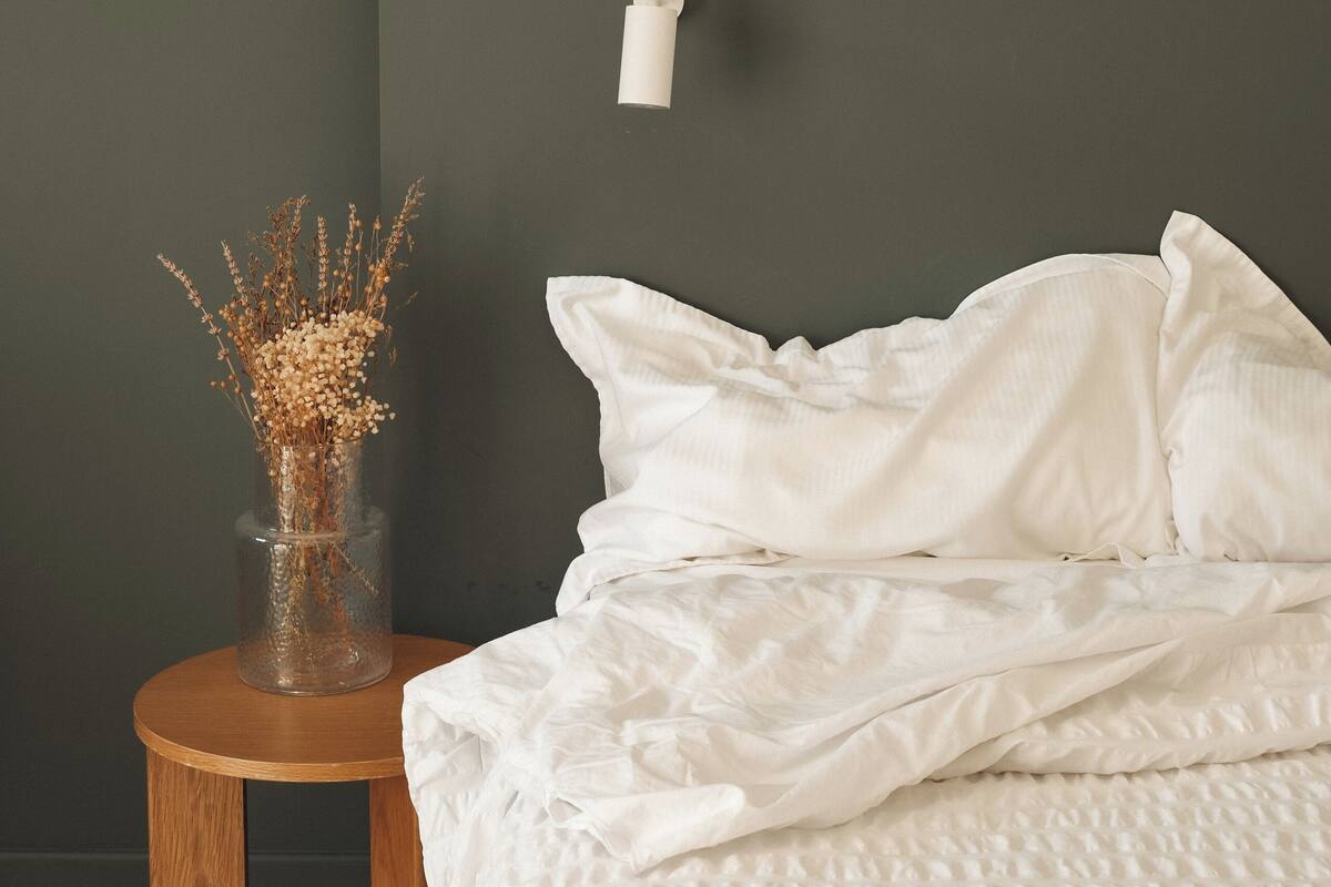 A bedroom with a bed, a bedside table with a vase, and a wall-mounted light fixture.