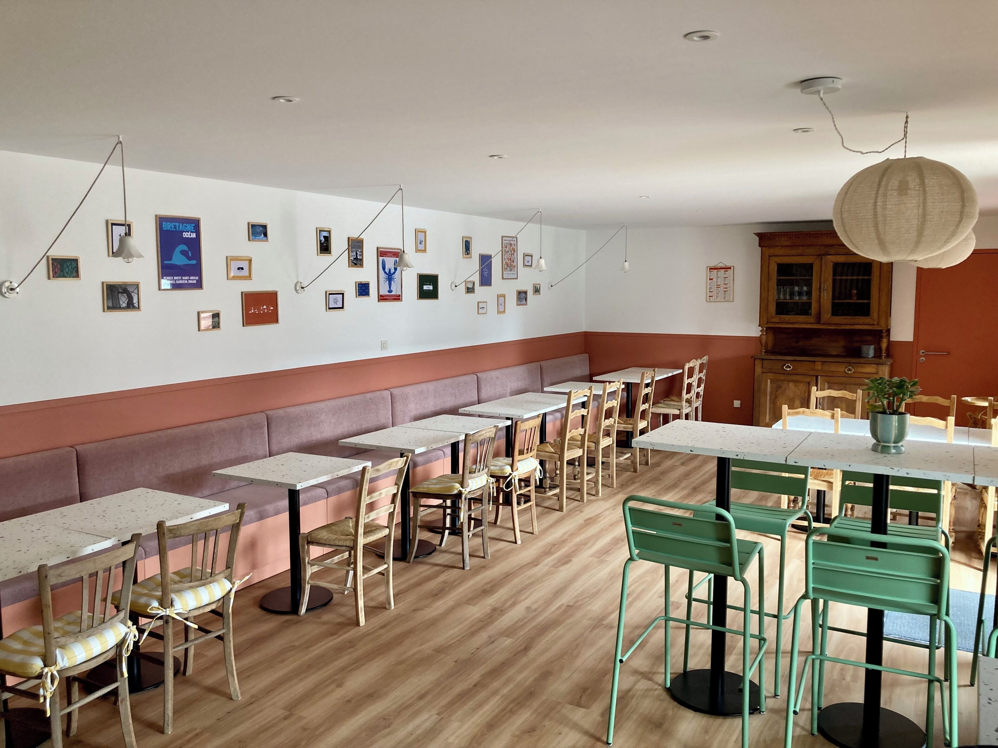 En restaurant med træborde og stole, en lang bænk og forskellige billeder i rammer på væggen.