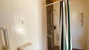 A bathroom with a toilet, a shower with a curtain, and a handrail.