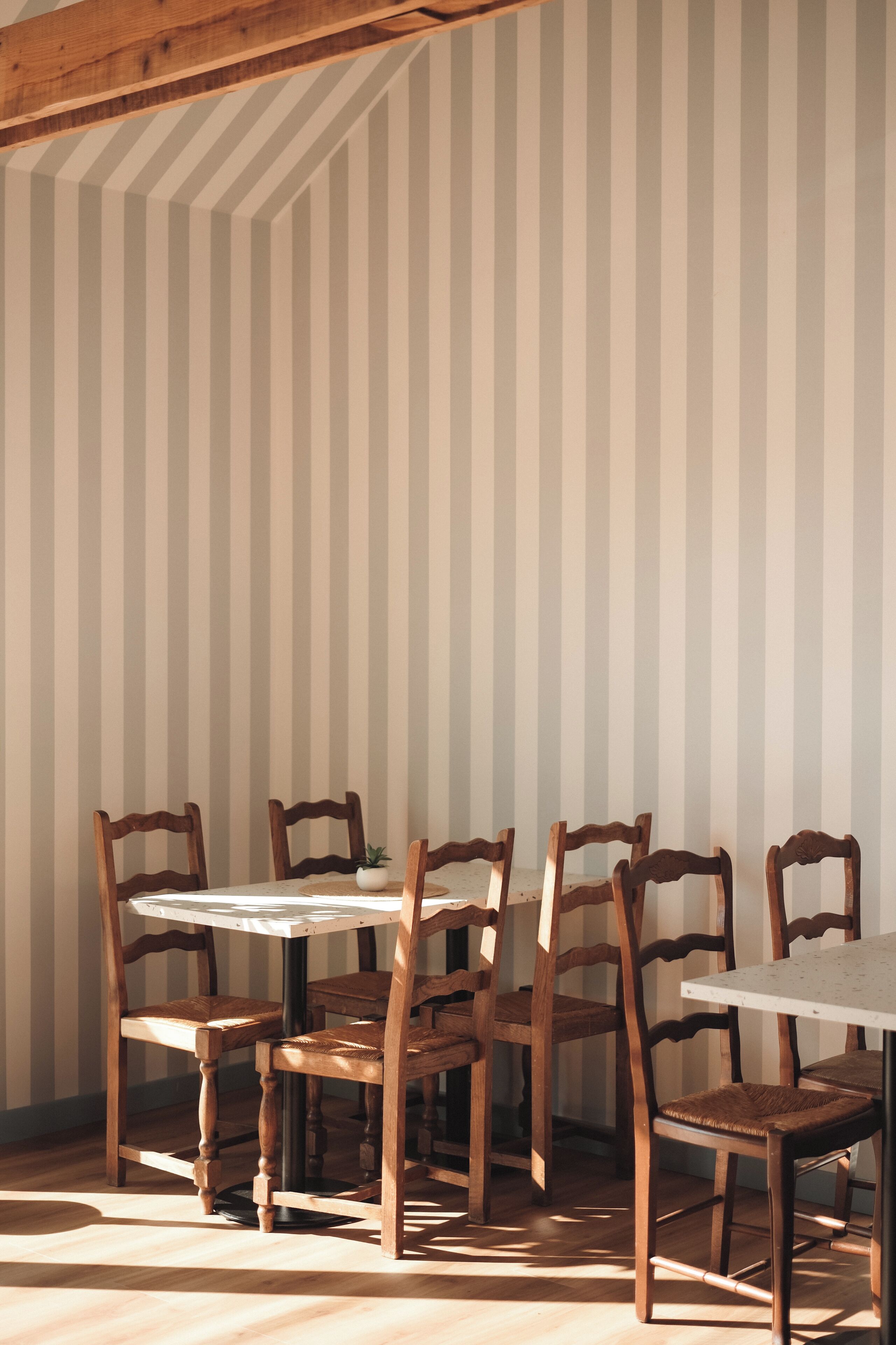 Un comedor con una mesa redonda y seis sillas de madera, un pared a rayas de fondo y una viga de madera en el techo.