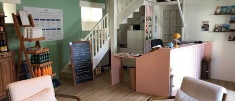 A cozy room with a wooden desk, two chairs, a chalkboard menu, and a staircase.