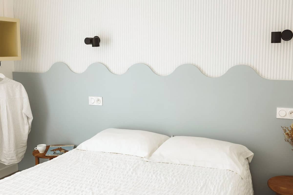 A neatly made bed with white bedding, a lamp on a bedside table, and a book.