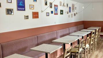 A restaurant with long wooden tables, cushioned benches, and framed pictures on the walls.