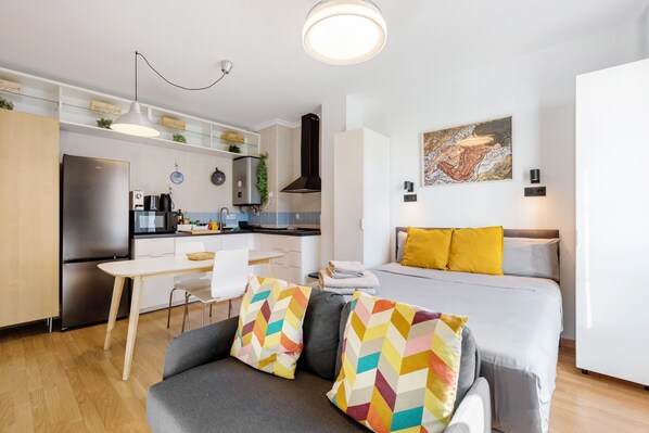 A modern apartment with a kitchenette, a dining area, and a living room with a sofa and a bed.