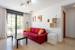 A living room with a red sofa, a small white side table, a glass door leading outside, and two framed pictures on the wall. - Apartment 'El Ático De La Montaña' with Balcony, Wi-Fi and Air Conditioning (Málaga)